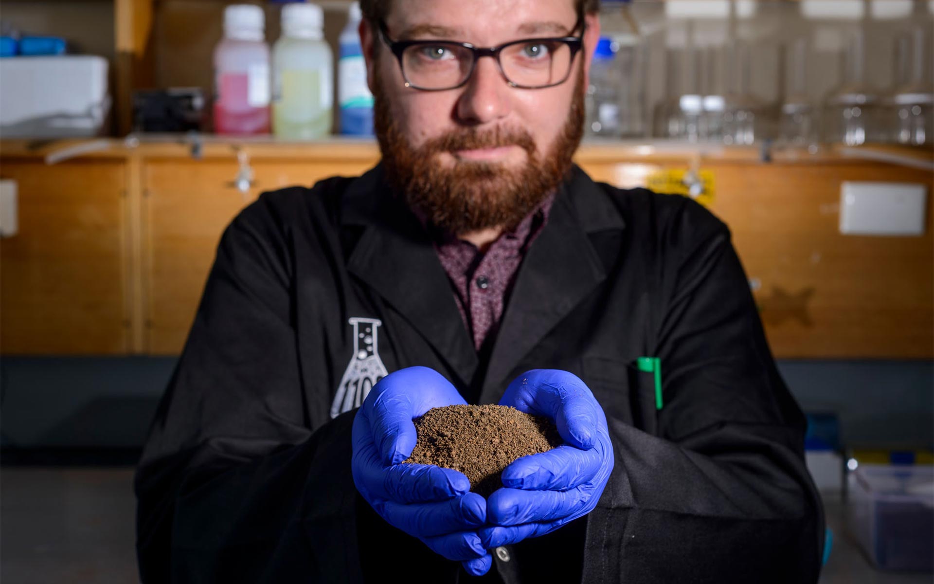 Scientist with gloved hands full of soil