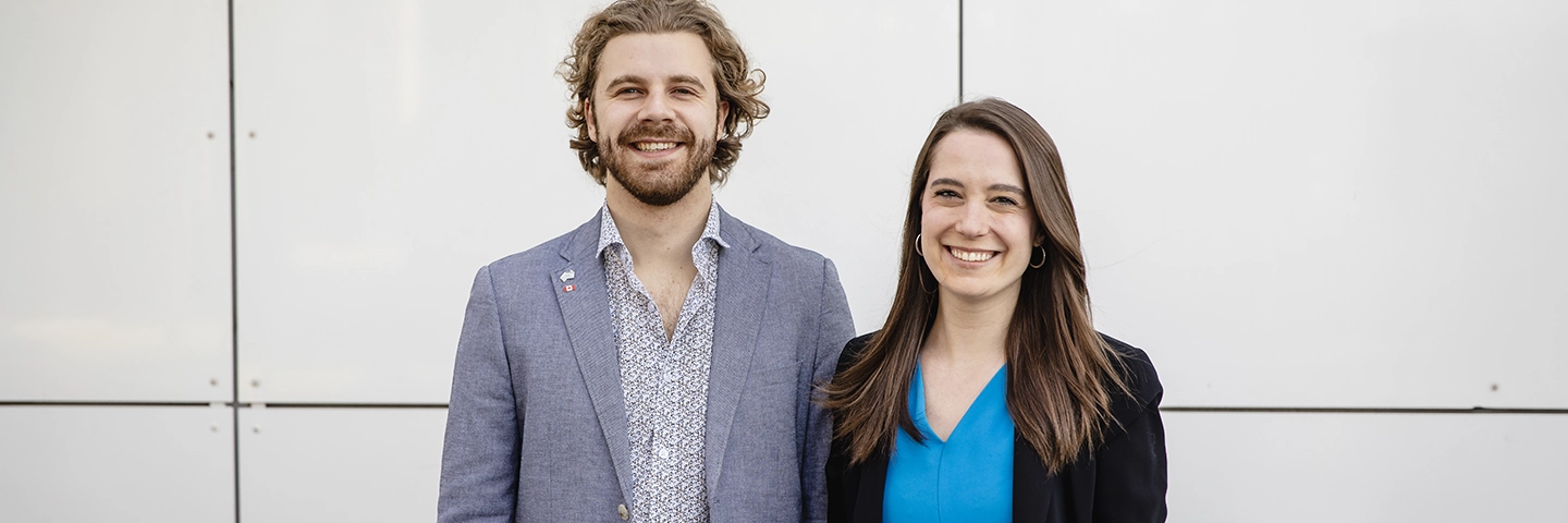 A male and female standing against a white background smiling