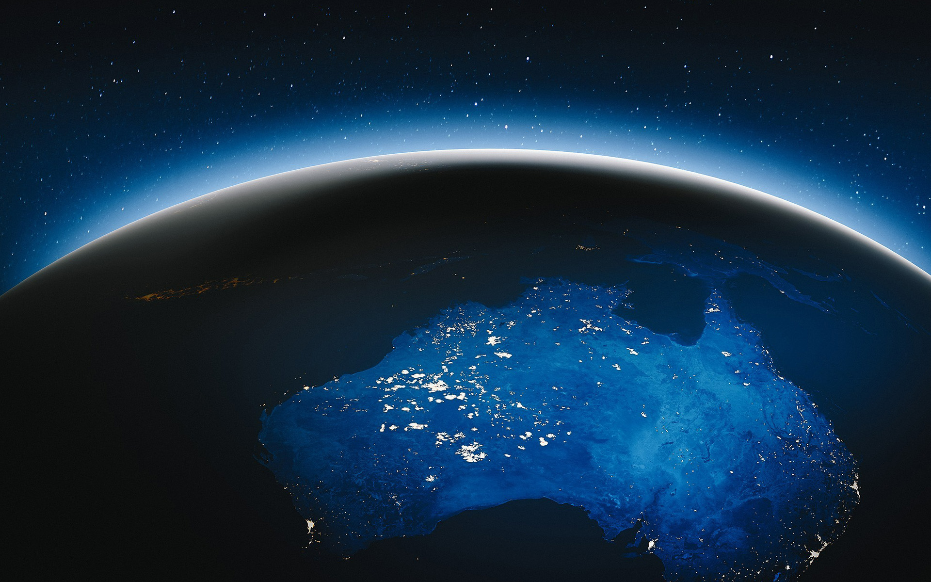 View of Australia from space at night, showing the continent illuminated in deep blue tones beneath a curved Earth horizon.